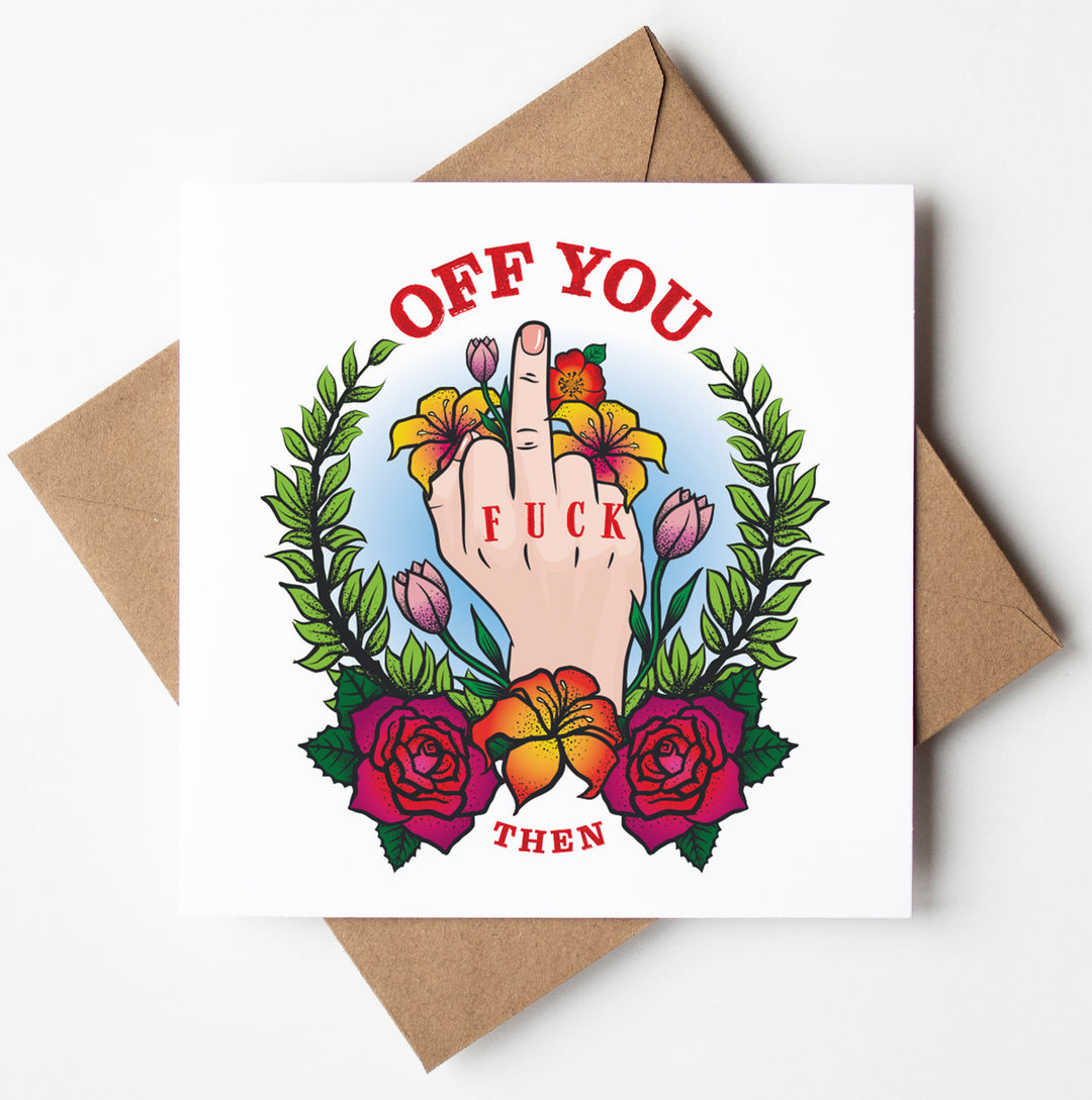 The "Off You Fuck Tattoo Card" features an illustration of a hand giving a middle finger, surrounded by vibrant flowers and leaves. The phrase "OFF YOU" appears above the hand, while "FUCK THEN" is displayed on the finger and below it. This humorous goodbye card is centered on a white card with a brown envelope included, and it comes with worldwide shipping.