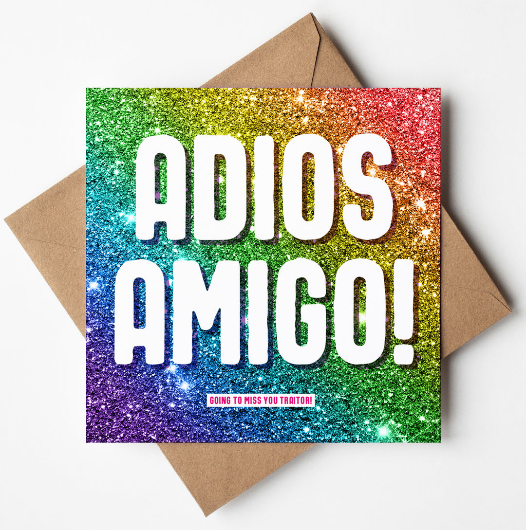 Colourful glitter greetings card with "ADIOS AMIGO!" in bold white letters and  small pink text saying "GOING TO MISS YOU TRAITOR!" beneath. The artwork is playfully placed on a brown envelope.