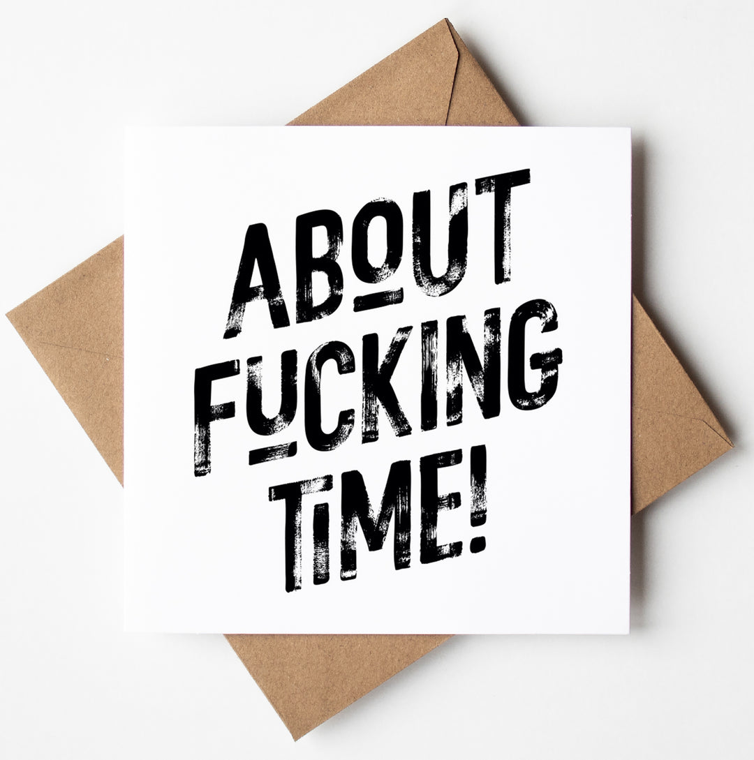 A square greetings card with a good luck message for your new job, boldly declares "ABOUT FUCKING TIME!" in striking black letters, nestled perfectly on a brown envelope.