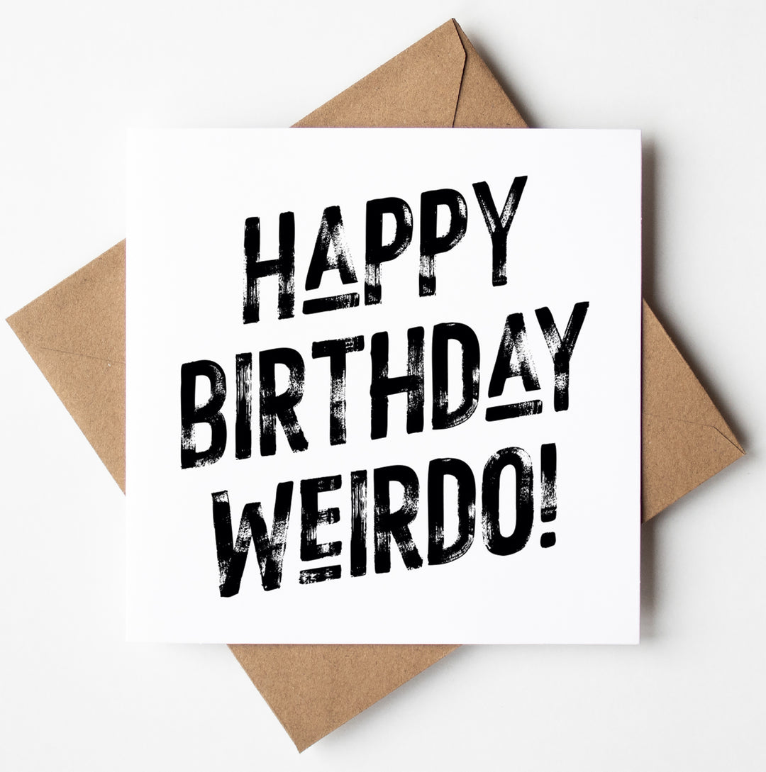 The Happy Birthday Weirdo! Harlem Card features bold black typography on a white background with the message "Happy Birthday Weirdo!" It is displayed atop a brown envelope against a plain white backdrop, ready for worldwide shipping.