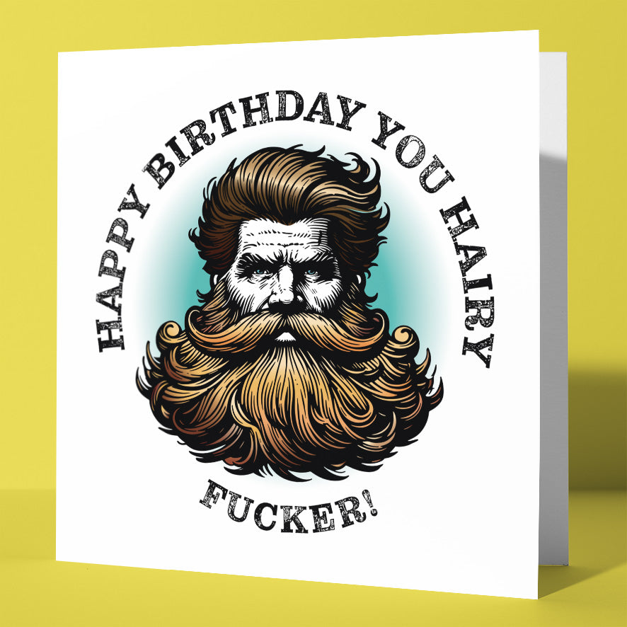 A UK-printed birthday card featuring an illustrated blonde man with thick, wavy hair. The sweary card reads "Happy Birthday You Hairy Fucker!" on a white background with a yellow surface. Product: Happy Birthday You Hairy Fucker! Blonde Card.