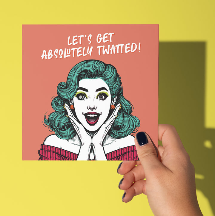 A hand with dark nail polish holds the "Let's Get Absolutely Twatted! Vintage Babes Birthday Celebration Card," featuring a surprised teal-haired woman and bold yellow background, perfect for a funny birthday. Designed in Wales.