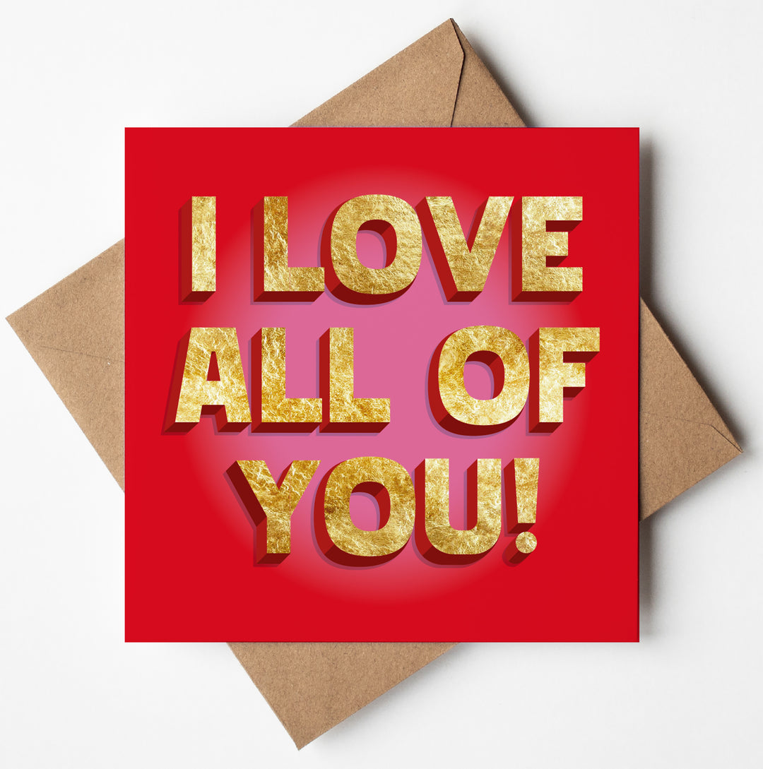 The "I Love All of You! Card" features bold, golden 3D letters on a red gold foil surface and rests elegantly against a white background with a brown envelope.