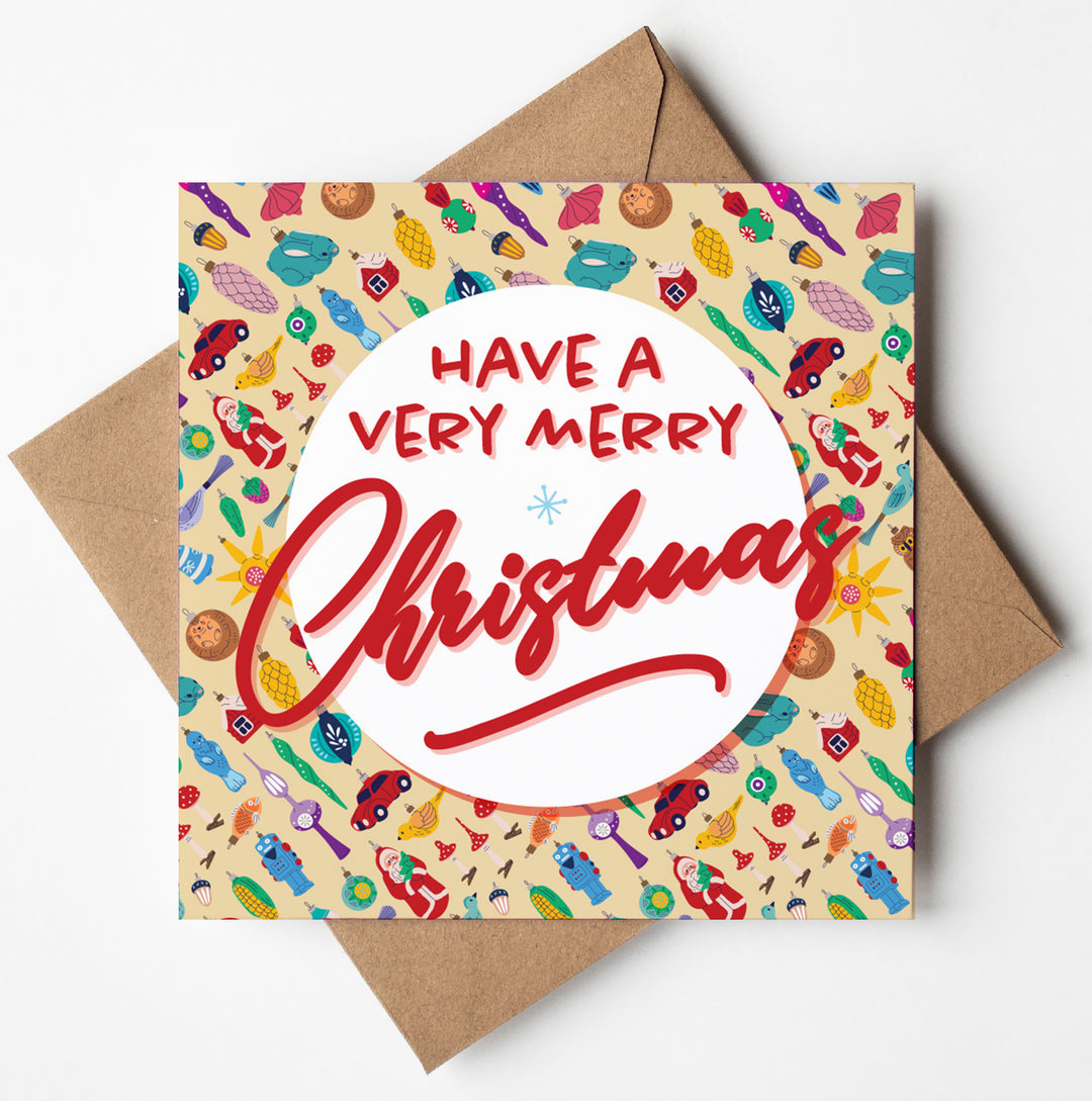 The Vintage Bauble Merry Christmas Card displays "Have a Very Merry Christmas" in bold red and white fonts on its cover, adorned with festive icons such as snowflakes, mittens, and retro Christmas ornaments. It comes with a brown envelope for an added charming touch.