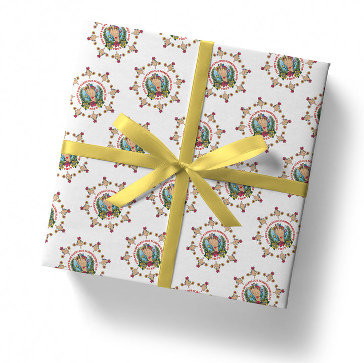 A square gift box wrapped in the SALE! Middle Finger Piss Off Tattoo Gift Wrap (Folded Sheet), featuring a colorful floral pattern and illustrated figure, tied with a yellow satin ribbon and bow, set against a plain white background.