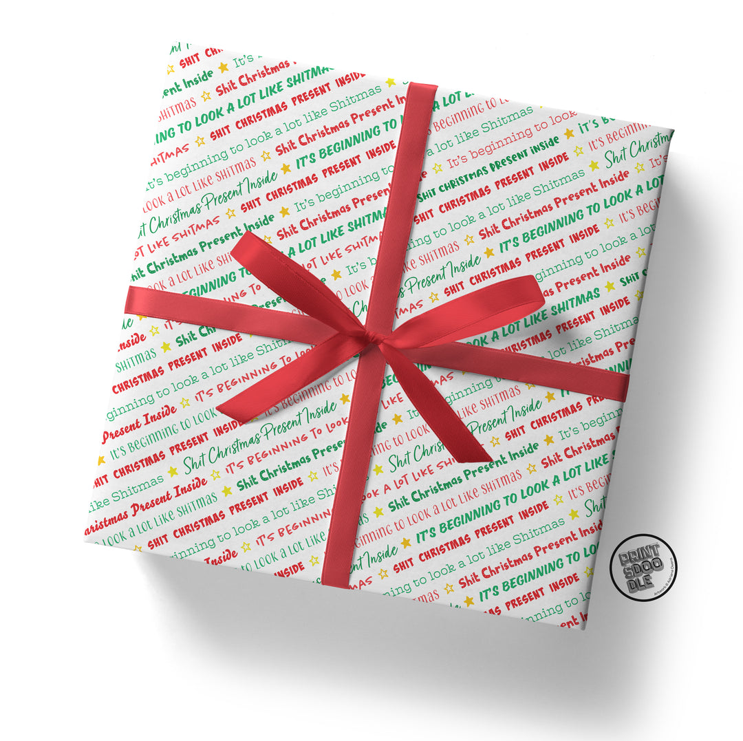 A square gift box wrapped in SALE! Funny 'Shit Christmas Present Inside' Gift Wrap, featuring playful holiday text in red, green, and yellow with small stars, topped with a bright red ribbon bow for a festive touch.