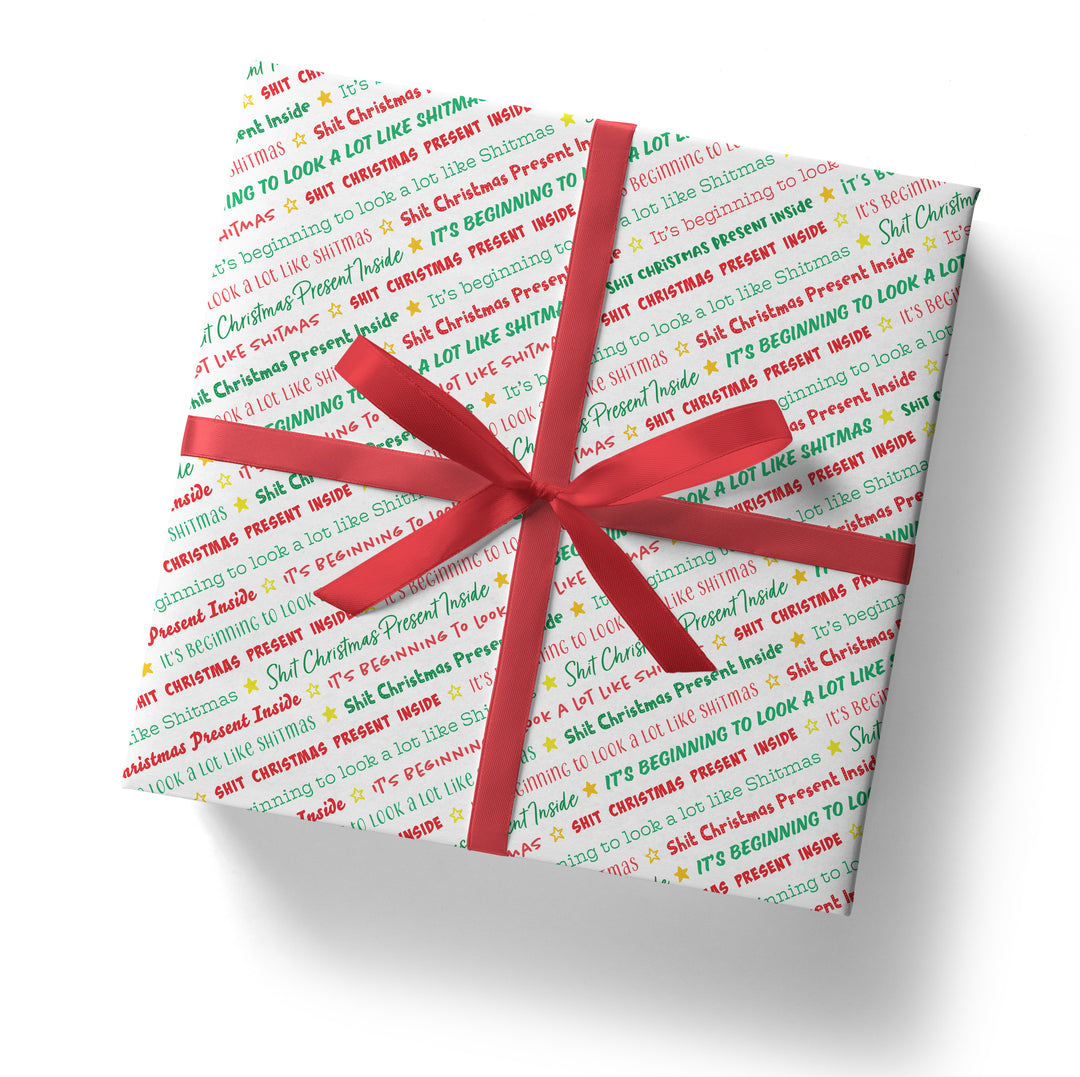 A square gift box wrapped in SALE! Funny 'Shit Christmas Present Inside' Gift Wrap, topped with a red ribbon and bow, is photographed on a white background.