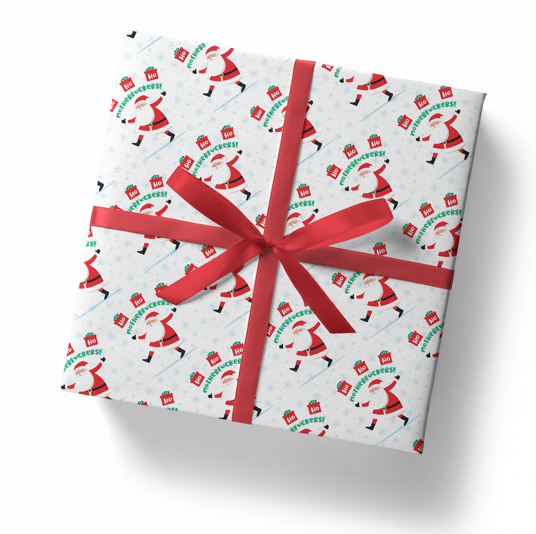 A square gift box wrapped in "SALE! Ho Ho Ho Motherfuckers!" folded sheet, decorated with a red ribbon and bow, featuring dancing Santa Claus and "Ho Ho Ho" signs, viewed from above on a white background.