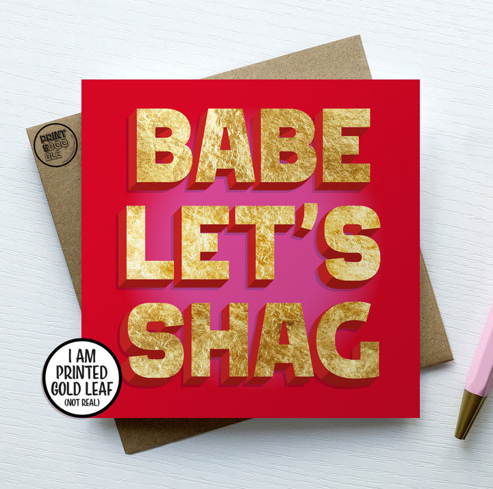 A square greetings card with a red and pink background with the words "BABE LET'S SHAG" in printed gold letters.