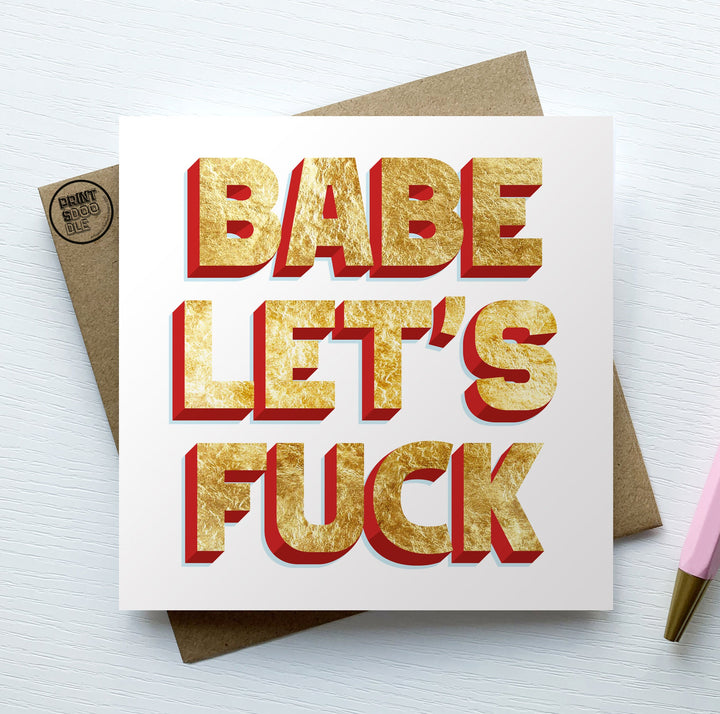 A "Babe Let's Fuck Love Card" with bold gold and red text is placed on a brown envelope. On the right, a pink pen peeks out, all set against a light, textured background.