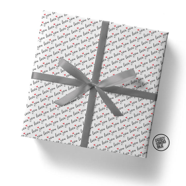 A gift wrapped in Love You Gift Wrap (Folded Sheet), which features the word "love" printed repeatedly in black and red, is elegantly tied with a shiny silver ribbon and bow. It's perfect for a boyfriend's birthday gift or any romantic occasion.