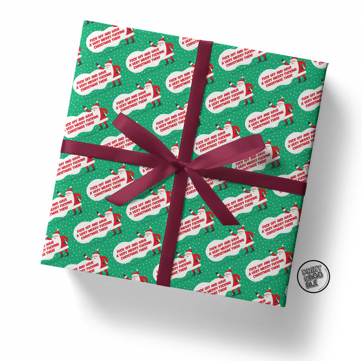 The wrapped gift displays a whimsical design from the "Fuck Off and Have a Very Merry Christmas Gift Wrap (Folded)" collection, featuring Santa illustrations with speech bubble messages. This Secret Santa wrap uses green paper adorned with white dots, complemented by a red bow to bring festive joy.