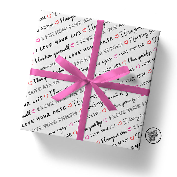 A square package, elegantly wrapped in the "I Love Your Dick" gift wrap, features a chic pattern of romantic phrases and small hearts in black, pink, and red on a white background. Accentuated with a large pink ribbon, this makes for an ideal Valentine's or birthday present for your boyfriend.